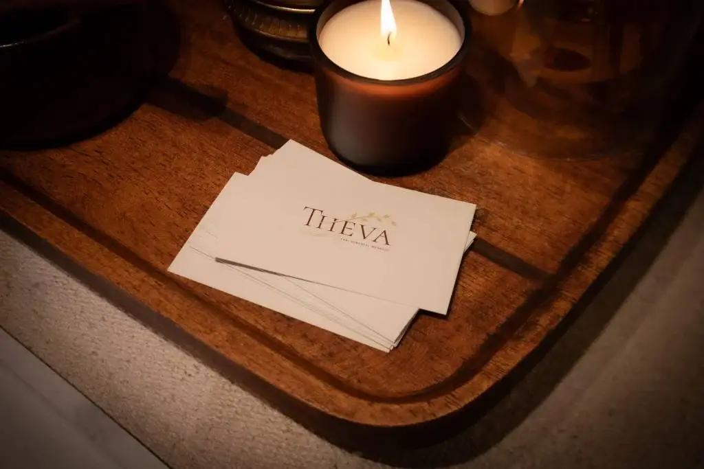THEVA Remedial business cards beside a lit candle on a wooden tray